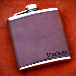 May include: A brown leather-covered flask with a silver metal body and a personalized inscription that reads "Parker".