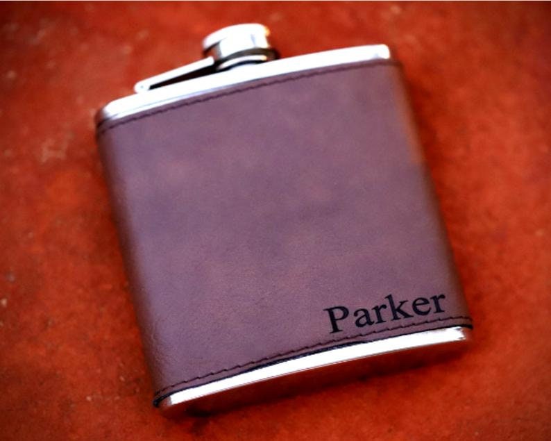 May include: A brown leather-covered flask with a silver metal body and a personalized inscription that reads "Parker".