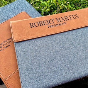 May include: Two brown leather laptop sleeves with personalized text. The top sleeve has the text "ROBERT MARTIN PRESIDENT" and the bottom sleeve has the text "Dad, You Are My Hero Thank You For A Love, Sarah".