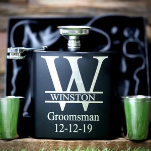 May include: Black flask with a silver funnel and two silver shot glasses. The flask is engraved with a large letter "W" and the text "Winston,  Groomsman, 12-12-19".