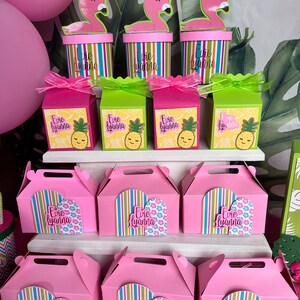 May include: Pink and green favor boxes with a flamingo and pineapple design. The boxes are labeled with the name "Evie Lyanna".