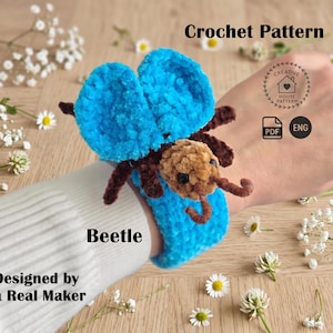 May include: A crochet pattern for a beetle, featuring a bright blue plush body with large wings and a brown head with dark eyes. The text reads Crochet Pattern, Beetle, Designed by a Real Maker, Creative House Pattern, PDF, and ENG.