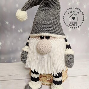 A crochet pattern gnome doll with a gray hat and body, white beard, and pink nose. The gnome has black and white striped legs and is wearing gray shoes.