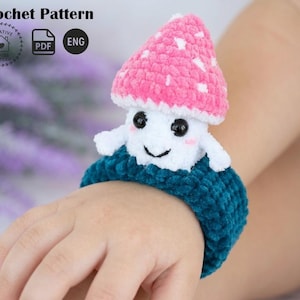 May include: A handmade crochet mushroom wristband with a smiling face and a pink and white cap. The wristband is teal and the mushroom has black eyes. The image also includes the text "Crochet Pattern".