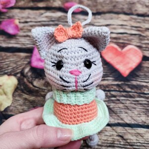 Peut inclure: Ornement de chat au crochet fait &agrave; la main en gris, orange et vert. Le chat a un nez rose, des yeux noirs et un petit n&oelig;ud orange. Le chat porte une robe verte et orange. L'ornement a une boucle blanche pour l'accrocher.