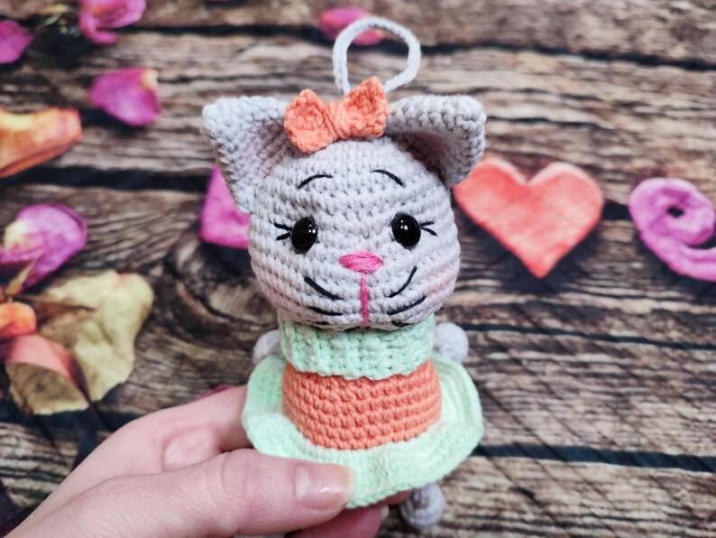 Peut inclure: Ornement de chat au crochet fait &agrave; la main en gris, orange et vert. Le chat a un nez rose, des yeux noirs et un petit n&oelig;ud orange. Le chat porte une robe verte et orange. L'ornement a une boucle blanche pour l'accrocher.