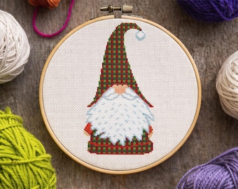 May include: A cross-stitch embroidery project in a circular wooden hoop featuring a gnome with a long white beard and a tall, pointed hat in a red and green plaid pattern. The gnome has a small peach-colored nose and a blue pom-pom on the hat.