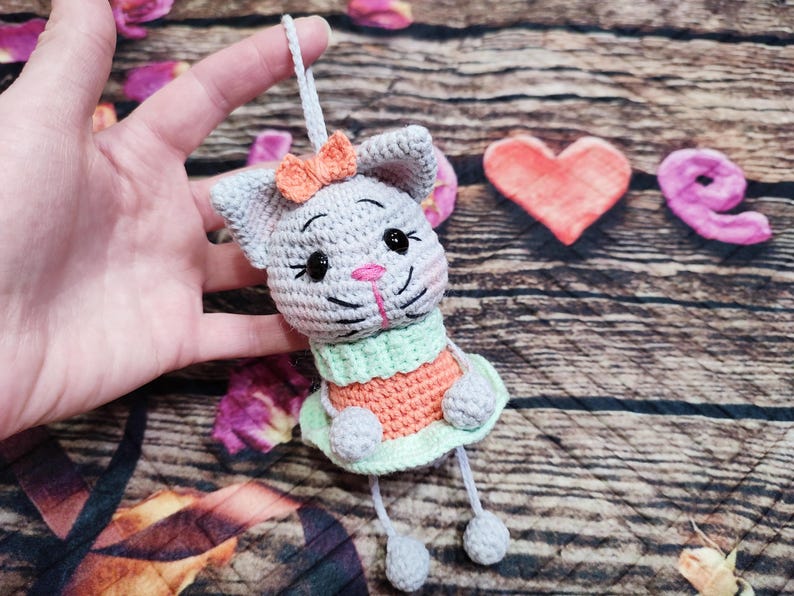 Peut inclure: Ornement de chat au crochet fait &agrave; la main en gris, orange et vert. Le chat a un nez rose et un petit n&oelig;ud orange. Le chat porte une robe verte et orange. Le chat est suspendu &agrave; une ficelle blanche.