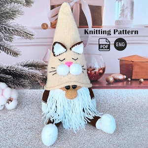 Pode incluir: Uma boneca de gnomo de malha com um rosto de gato no chapéu. O chapéu é bege com orelhas castanhas e um nariz rosa. O gnomo tem barba branca, braços e pernas castanhas e pés brancos. O texto "Knitting Pattern" é visível.