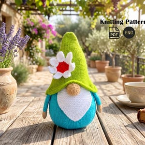 May include: A knitted gnome with a green hat, white beard, and blue body, adorned with a white and red flower. The image includes the text "Knitting Pattern" and a PDF/ENG icon.