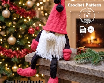 May include: A crochet pattern for a gnome featuring a tall red hat with two black pom-poms, a white yarn beard, black arms and legs, and red mittens and shoes. The text reads Crochet Pattern, Creative House Pattern, PDF, ENG, and Real Handmade Designs.