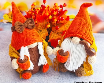 May include: Two crochet gnomes with orange hats, white beards, and brown bodies. One gnome has a bow tie, the other a pipe. Both hold small orange pots. They wear yellow scarves. The background features fall foliage.