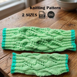 May include: Two knitted green arm warmers with a cable knit design and turquoise trim. The image includes the text "Knitting Pattern", "2 SIZES", "PDF", and "ENG". The arm warmers are displayed on a wooden surface.