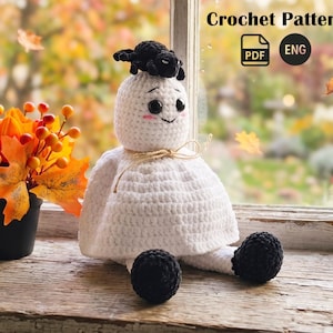 Könnte beinhalten: Geisterpuppe aus weißer Häkelarbeit mit einer schwarzen Spinne auf dem Kopf, schwarzen Knopfaugen und rosigen Wangen. Die Puppe hat schwarze Kugelfüße und ist mit Bindfaden gebunden. Der Text "Crochet Pattern" und ein PDF/ENG-Symbol sind enthalten.