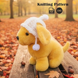 May include: A yellow plush dog toy wearing a white knitted hat with a pom-pom. The image includes the text "Knitting Pattern" and PDF and ENG icons. The dog is sitting on a wooden surface with acorns and autumn leaves.