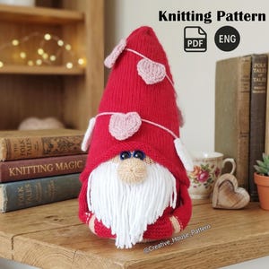 Puede incluir: Un gnomo tejido a mano de color rojo con barba blanca, ojos azules y una guirnalda de corazones rosas. El gnomo lleva un gorro rojo y tiene una nariz beige. La imagen también incluye el texto "Knitting Pattern".