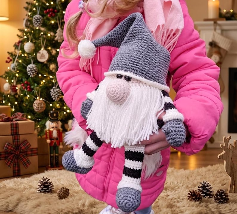 A crochet pattern gnome doll with a gray hat and body, white beard, and pink nose. The gnome has black and white striped legs and is wearing gray shoes.