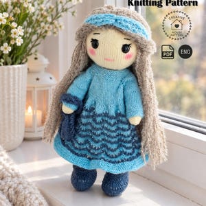 May include: A knitted doll with long beige hair, a blue headband, and a blue dress featuring a wavy pattern. The doll has black eyes and pink cheeks. Text on the image reads Knitting Pattern, Creative House Pattern, PDF, and ENG.