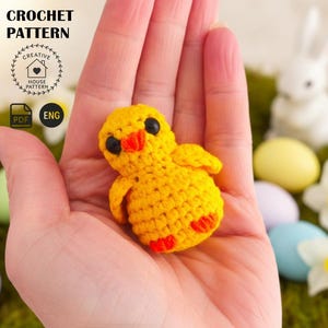 Könnte beinhalten: Ein gehäkeltes gelbes Küken mit orangefarbenen Akzenten, gehalten in einer Hand. Das Küken hat schwarze Augen und ist Teil eines Häkelmusters. Das Bild enthält den Text "CROCHET PATTERN" und ein Logo mit den Worten "CREATIVE HOUSE PATTERN".