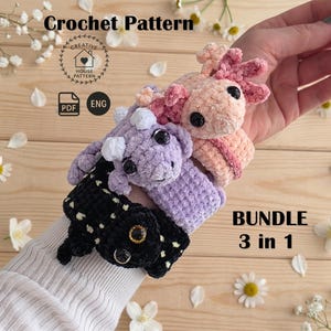 May include: A crochet pattern bundle featuring three plush axolotl toys in pink, purple, and black. The text reads Crochet Pattern, PDF, ENG, and BUNDLE 3 in 1. Each axolotl has black safety eyes and textured yarn bodies with external gills.