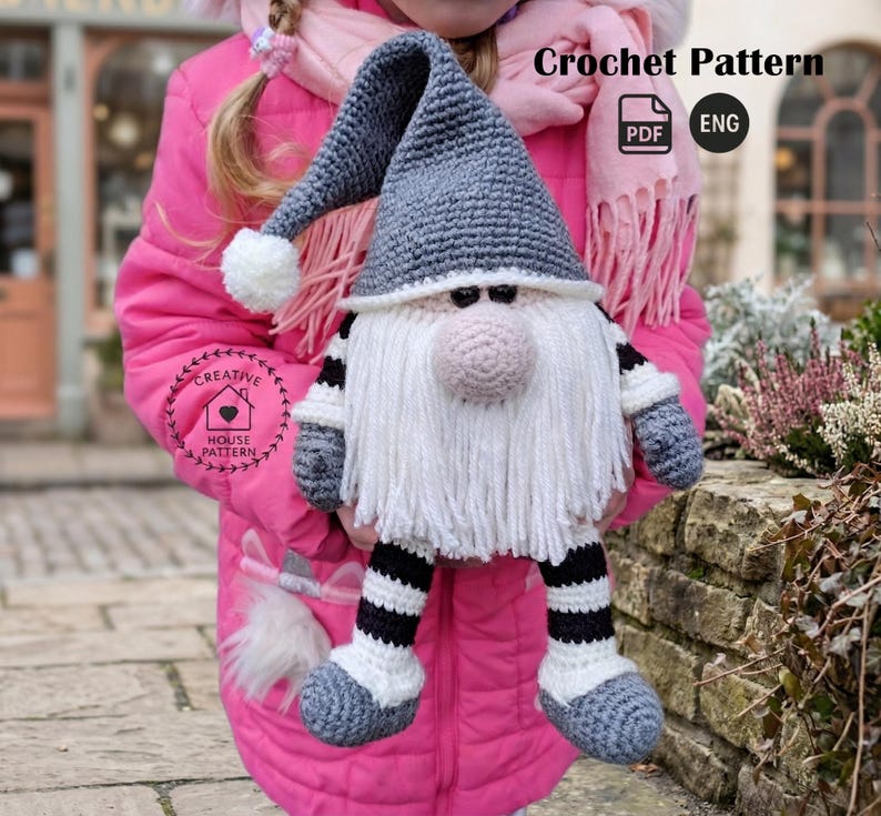 A crochet pattern gnome doll with a gray hat and body, white beard, and pink nose. The gnome has black and white striped legs and is wearing gray shoes.