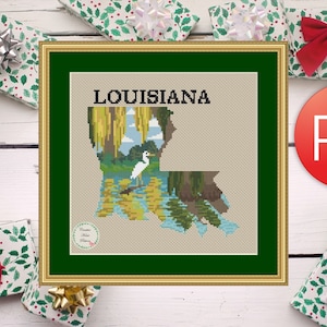 Puede incluir: Un patrón de punto de cruz del estado de Luisiana con una garceta blanca de pie en una zona pantanosa. El patrón está enmarcado en un marco dorado con un passe-partout verde. El título "LOUISIANA" está impreso sobre el patrón.