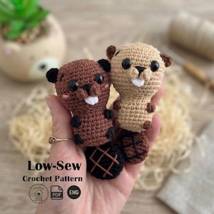 May include: Two handmade crochet beaver dolls. One is brown, the other is tan. Both have black eyes, black ears, and white teeth. The beavers are held in a hand. The text "Low-Sew Crochet Pattern" is at the bottom of the image.