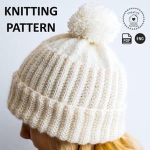 May include: A white knitted beanie with a ribbed texture and a large pom-pom on top. The image includes the text KNITTING PATTERN, a Creative House Pattern logo, a PDF icon, and the letters ENG, indicating a digital English language pattern.