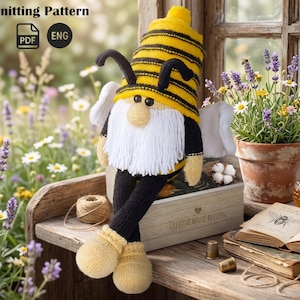 May include: A knitted bee gnome pattern. The gnome features a yellow and black striped hat, black antennae, and a white beard. It wears a black top, black trousers, and yellow shoes. The text "Knitting Pattern" and "ENG" are visible.