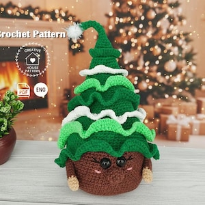 Può includere: Uno schema all'uncinetto per un peluche a forma di albero di Natale con base marrone, livelli verde scuro e dettagli bianchi arricciati. Il giocattolo presenta occhi in plastica nera, guance ricamate in rosa e un pompon bianco sulla punta.