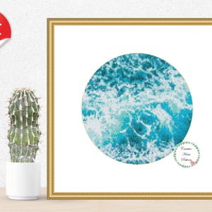 May include: A digital cross stitch pattern featuring a circular design of blue and white ocean waves. The pattern is framed in a gold frame and displayed on a white wall.