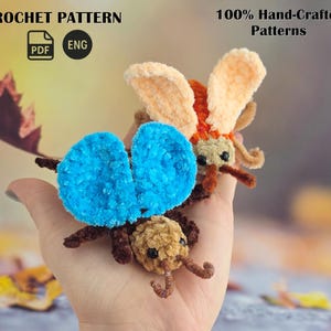 Puede incluir: Dos pequeñas figuras de insectos de ganchillo, de felpa, con texturas difusas. Una tiene alas azul brillante y cabeza beige, mientras que la otra tiene alas naranja claro y cabeza beige. Texto: CROCHET PATTERN, PDF, ENG, 100% Hand-Crafted Patterns.