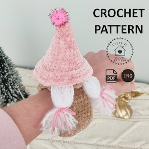 May include: Crochet pattern for a pink and brown gnome wrist cuff. The pattern is available in PDF format and is in English. The pattern is called "Creative House Pattern".