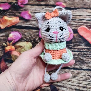 Peut inclure: Lapin crochet&eacute; gris avec un n&oelig;ud orange, un nez rose et des yeux noirs. Le lapin porte une tenue verte et orange avec une jupe vert clair. Il est fait &agrave; la main et a des jambes pendantes avec des pompons gris.