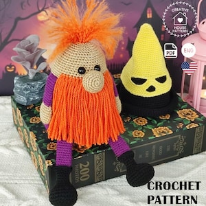 May include: A handmade crochet gnome with an orange beard, orange hair, and purple accents. Next to it is a yellow crochet hood with a black face. The words "CROCHET PATTERN" are at the bottom.