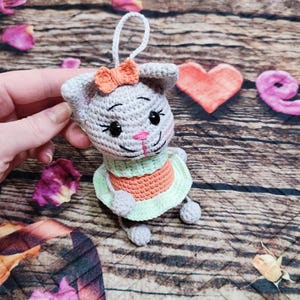 Peut inclure: Ornement de lapin en crochet gris fait &agrave; la main, avec un n&oelig;ud p&ecirc;che, des yeux noirs et un nez rose. Le lapin porte une robe verte et orange. L'ornement a une ficelle blanche pour l'accrocher.