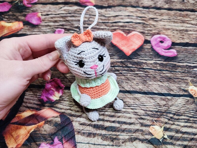 Peut inclure: Ornement de lapin en crochet gris fait &agrave; la main, avec un n&oelig;ud p&ecirc;che, des yeux noirs et un nez rose. Le lapin porte une robe verte et orange. L'ornement a une ficelle blanche pour l'accrocher.