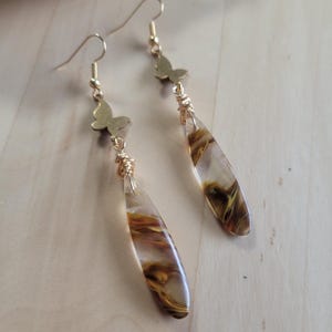 Könnte beinhalten: Goldene Schmetterlings-Ohrringe mit braunen und goldenen Agat-Tropfen.