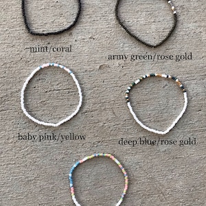 May include: Five beaded bracelets in different color combinations. The bracelets are made with small white beads and feature different colored beads, including mint, coral, army green, rose gold, baby pink, yellow, deep blue, and frost.