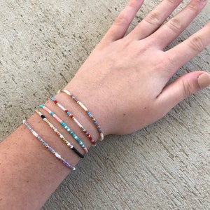 May include: A set of six colorful beaded bracelets on a person's wrist. The bracelets are made with small, colorful beads and are stacked on top of each other.