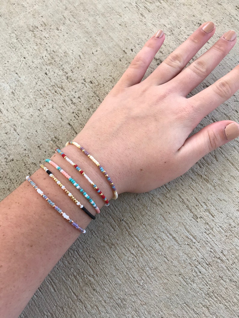 May include: A set of six colorful beaded bracelets on a person's wrist. The bracelets are made with small, colorful beads and are stacked on top of each other.