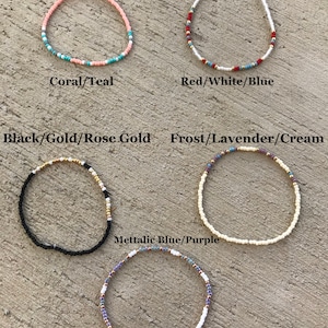 May include: Six different beaded bracelets with various color combinations. The bracelets are laid out on a textured surface. The colors include coral, teal, red, white, blue, black, gold, rose gold, frost, lavender, cream, metallic blue, and purple.
