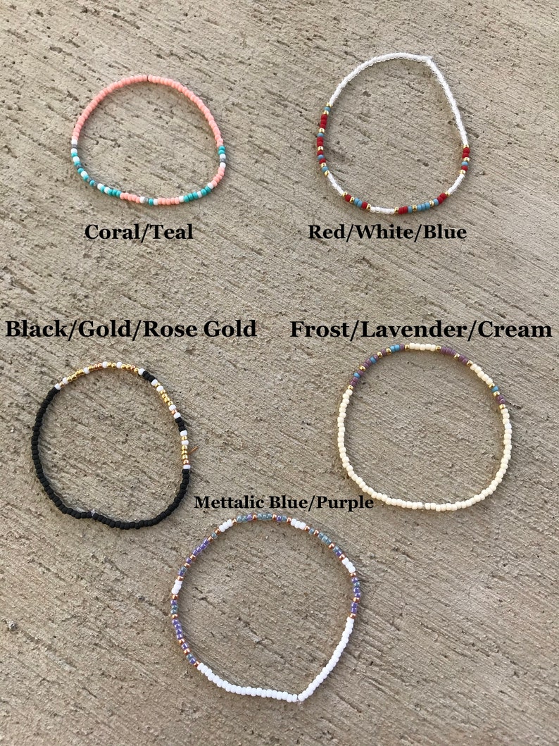 May include: Six different beaded bracelets with various color combinations. The bracelets are laid out on a textured surface. The colors include coral, teal, red, white, blue, black, gold, rose gold, frost, lavender, cream, metallic blue, and purple.