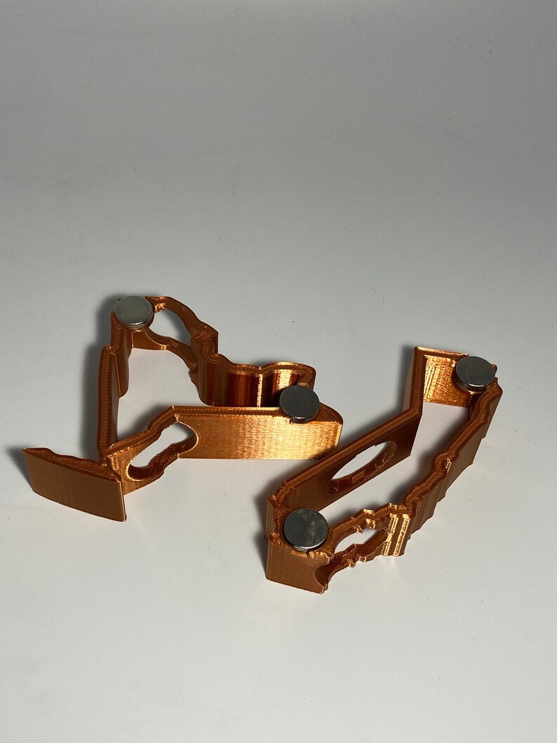 Puede incluir: Dos clips magn&eacute;ticos impresos en 3D, de color cobre, con un dise&ntilde;o decorativo. Cada clip tiene un peque&ntilde;o im&aacute;n redondo plateado en la parte inferior.