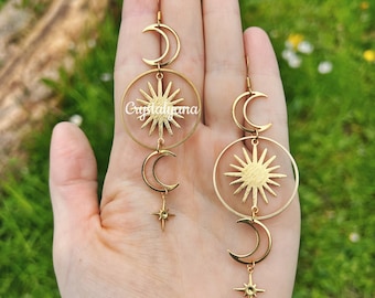 May include: Gold tone earrings with a sun and moon design. The earrings feature a circle with a sun design, a crescent moon, and a star charm.