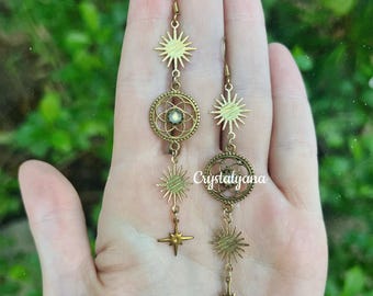 May include: A pair of long, dangling earrings in an antique brass finish. Each earring features a sunburst charm, a circular filigree medallion with a central iridescent stone, another sunburst, and a four-pointed star charm at the base.