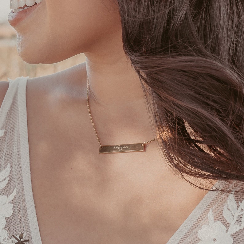 May include: A gold necklace with a bar pendant engraved with the name "Megan".