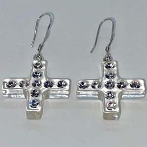 May include: A pair of silver earrings with a cross design. Each cross is adorned with clear rhinestones.