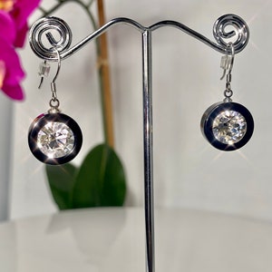 May include: A pair of silver dangle earrings with a black and clear crystal design. The earrings are hanging from a silver stand.