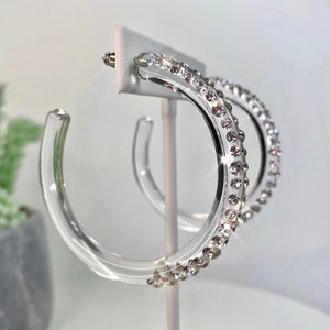 May include: Clear acrylic hoop earrings with a row of clear rhinestones around the edge.